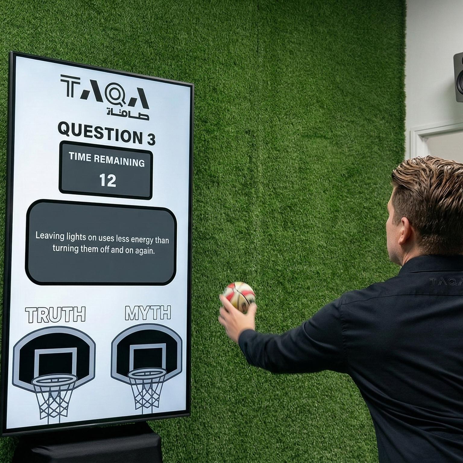 A guest throwing a softball at a large digital Truth or Myth display screen to lock in an answer at a high-energy corporate exhibition booth activation